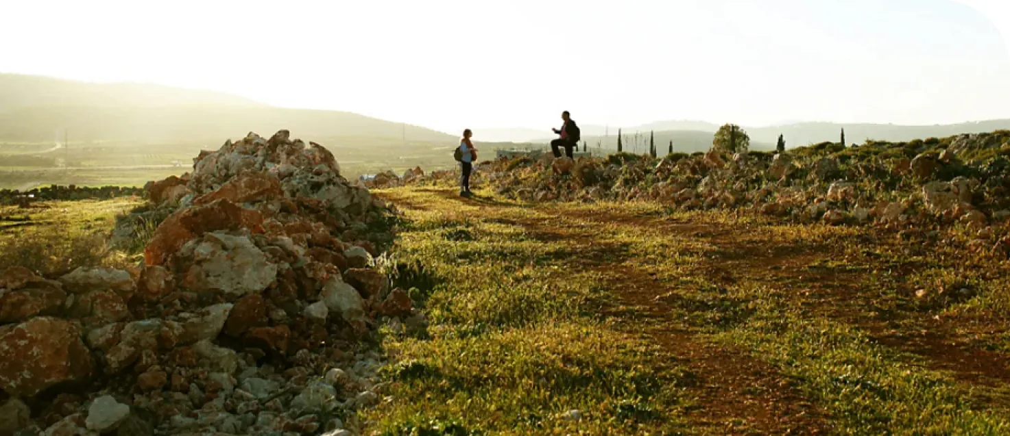 Archaeological landscape in Israel with ancient stone ruins and two people exploring at golden hour